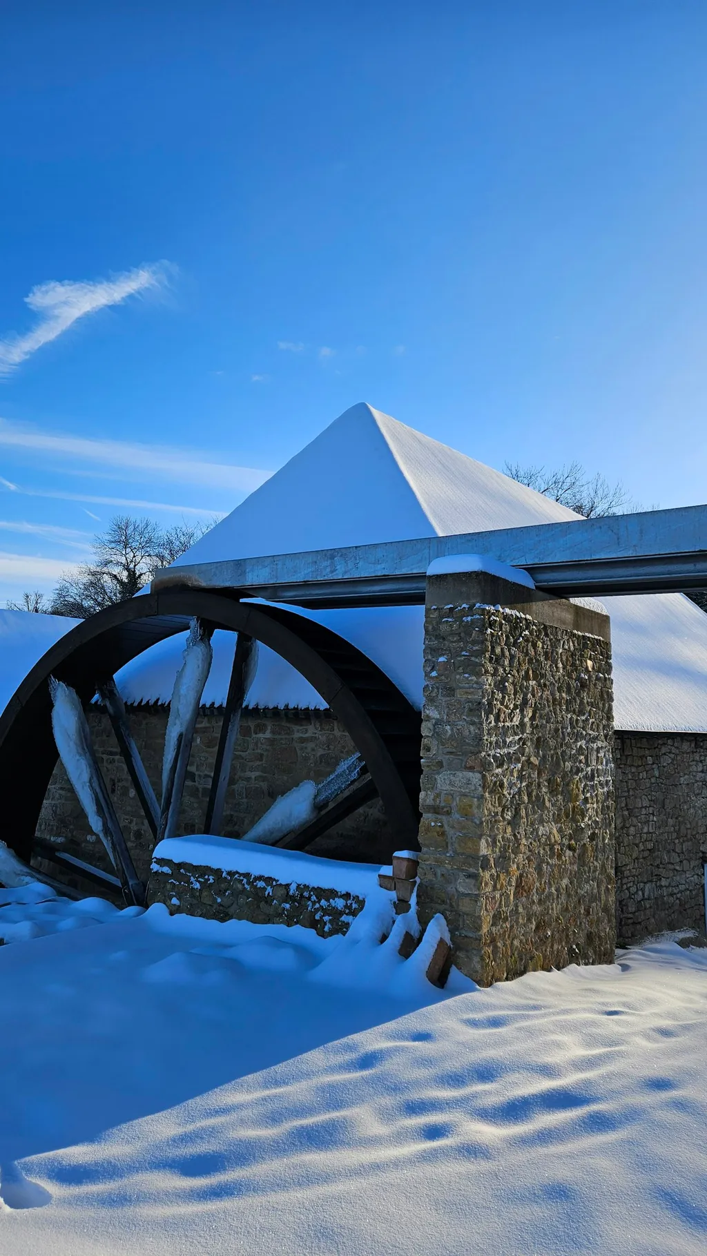 Das Mühlengebäude mit schneebedecktem Dach. Das Wasserrad läuft auch im Winter.